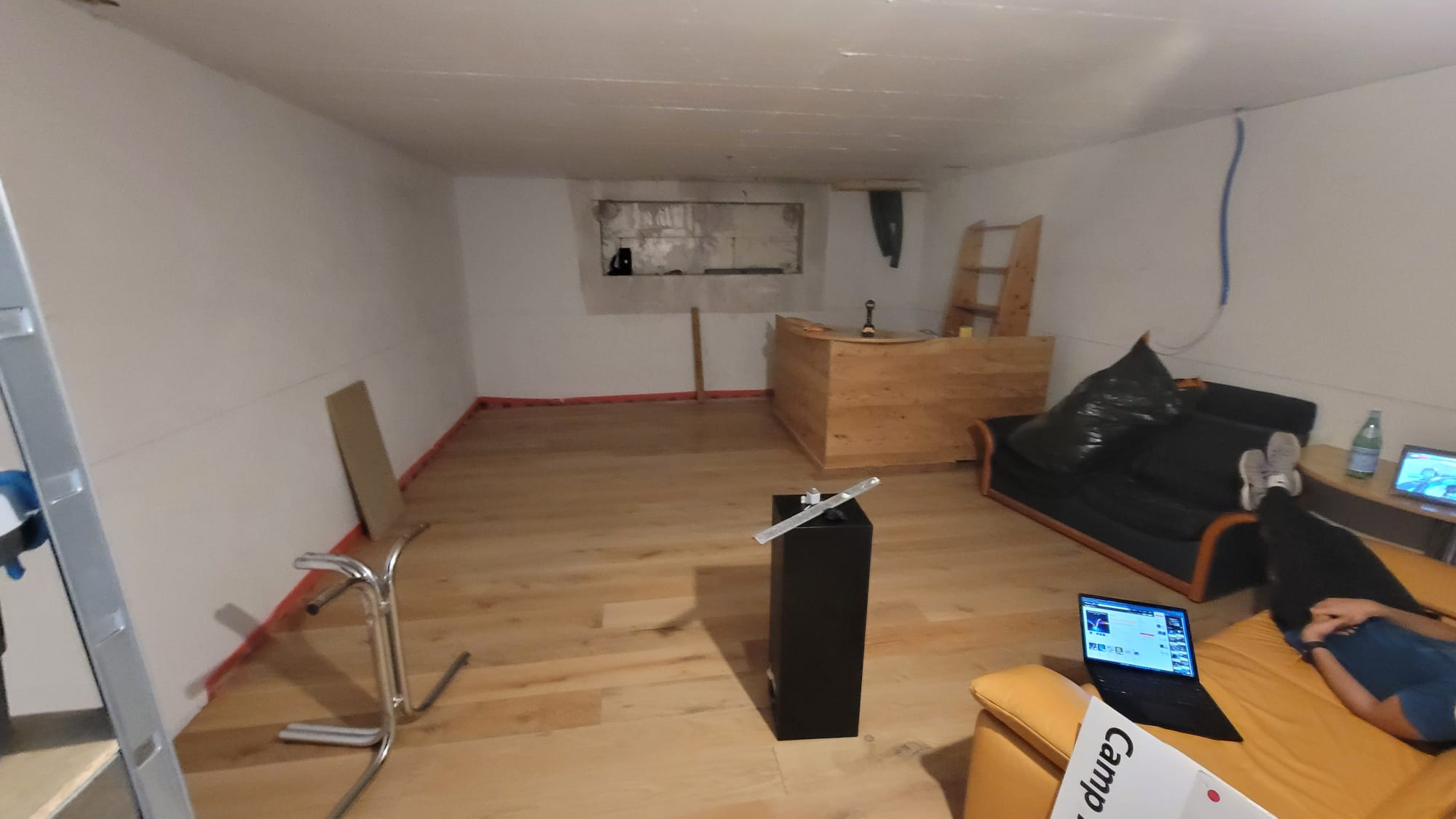 The cellar before the build: white walls, wood floor, the bar frame going in.