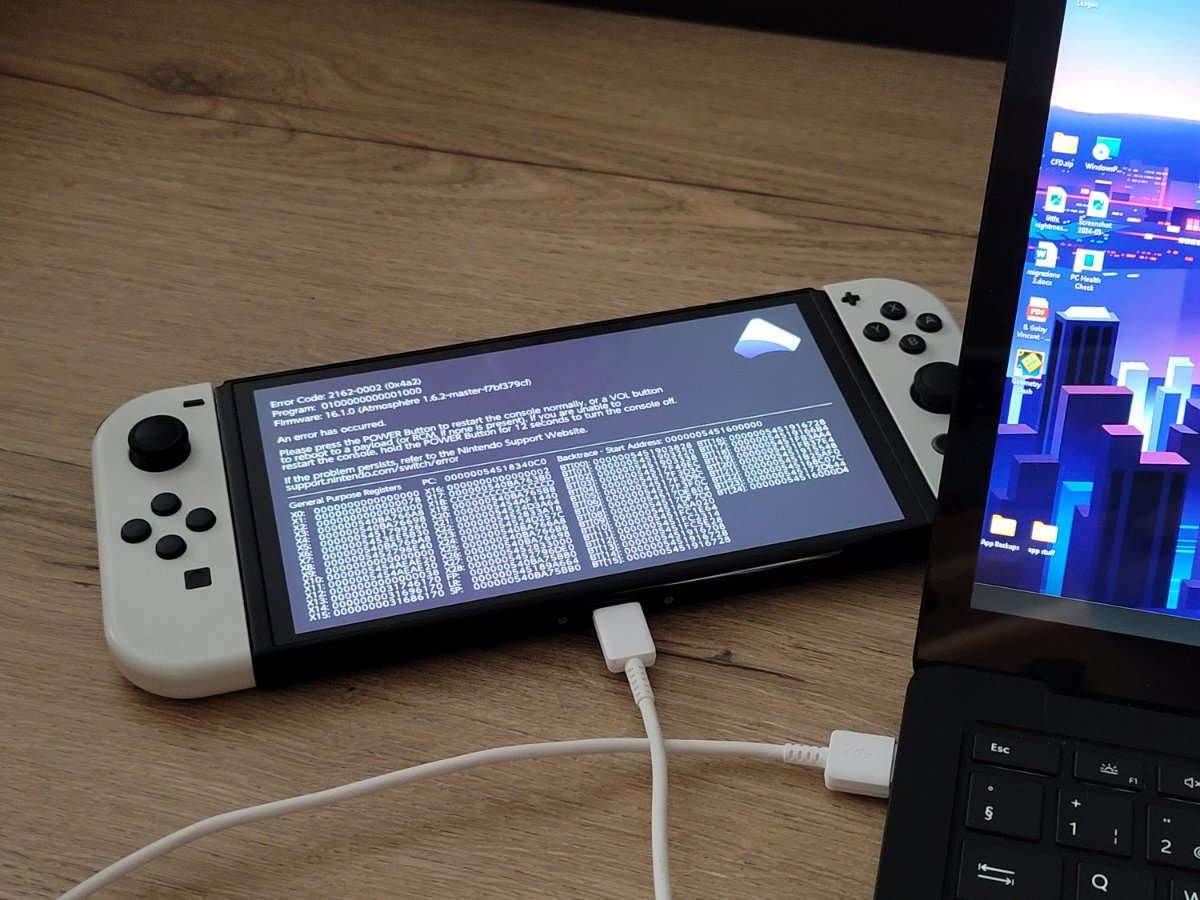 The console showing an Atmosphère crash dump with registers and a backtrace, tethered to a laptop.